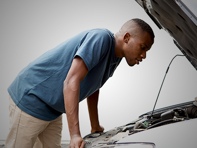 A man in a blue shirt looking at the engine of a white vehicle