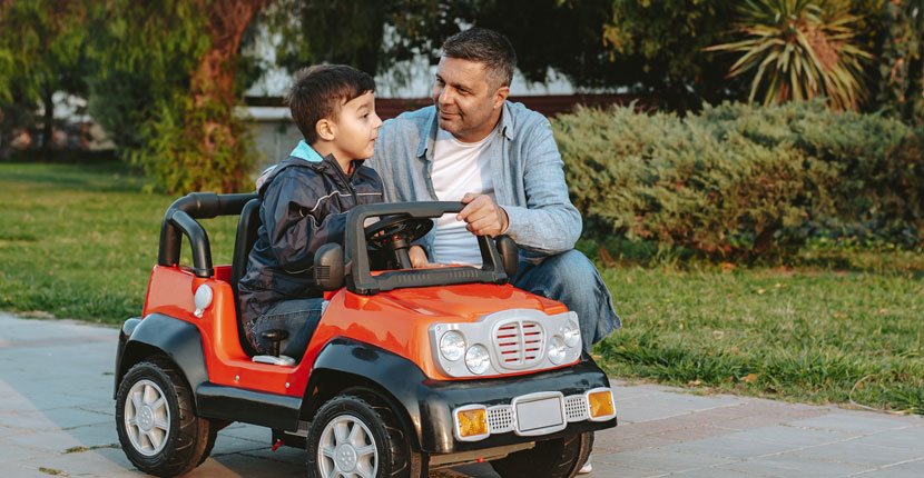 little boy in a toy riding car with father kneeling beside it