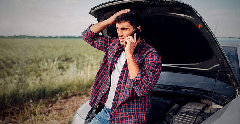 A man on the phone leaning against a car with its hood open