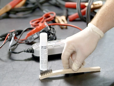 A person cleaning a battery with battery terminal spray and battery cleaner