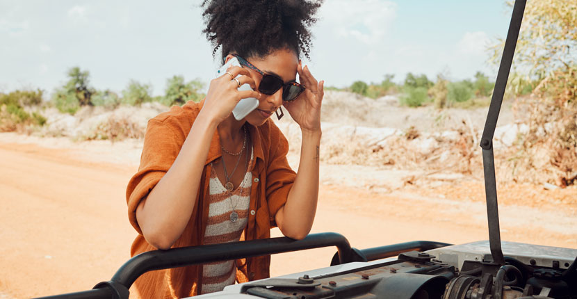 Woman in an orange top on the phone looking under the hood of a vehicle
