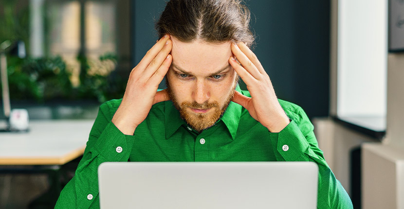 Man wearing green looking upset at his macbook