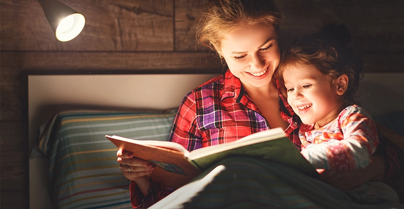 Woman and child reading a book in bed with a light