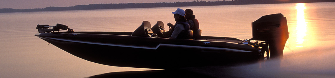 2 people on a black boat speeding through water at sunset