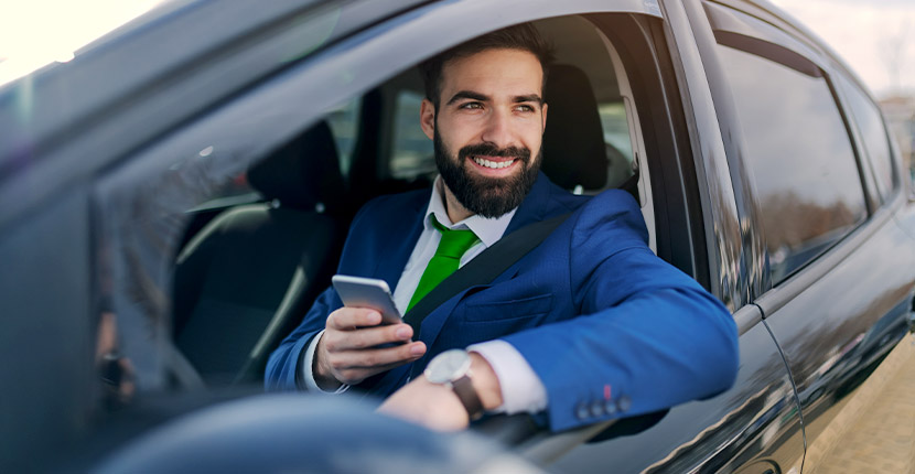 Man holding a phone dressed in a suit while sitting in a vehicle