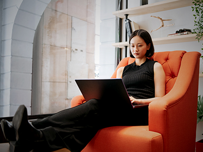 A woman sitting in an orange chair with a laptop on her lap