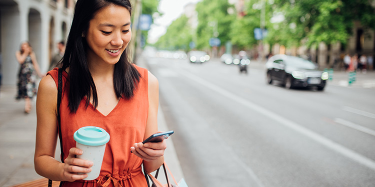 Woman on the sidewalk holding a cup of coffee and looking at her phone