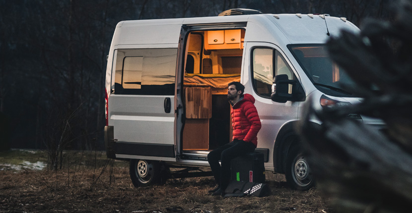 A man in a red coat sitting out side a camper van
