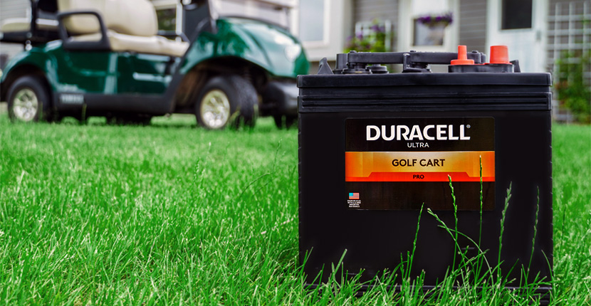 Golf cart battery on grass with a golf cart and house behind it