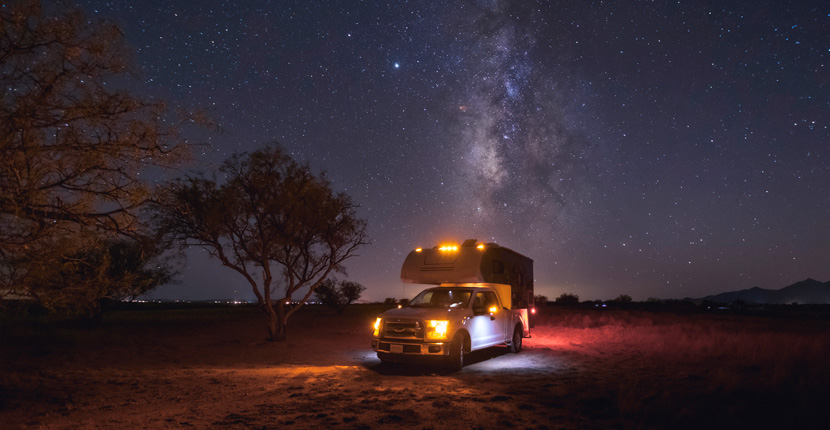 Pickup with a camper attachment lit up at night in a field under a starry sky