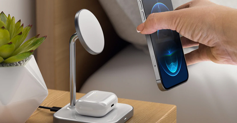 Person placing a phone on a MagSafe wireless charger with AirPods charging on the base