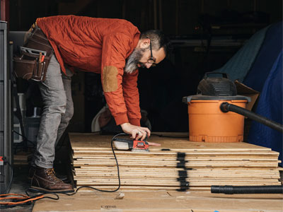 Contractor using an electric sander on some wood with a shop vac on the wood pile