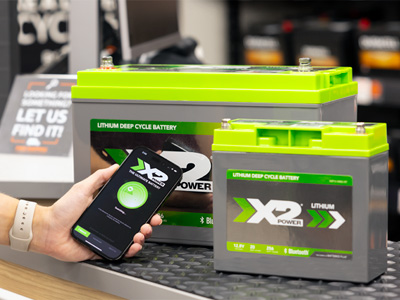 Two X2Power Marine batteries with Bluetooth and someone holding a phone with the app