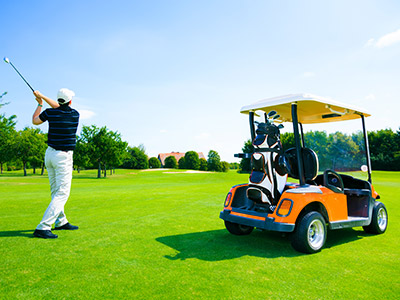 golfer finishing a swing next to a golf cart