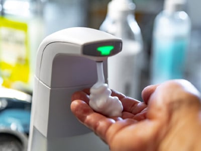 Hand gathering foam hand sanitizer from a touchless sanitizing station