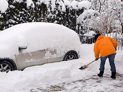 person shoveling out a white vehicle in winter