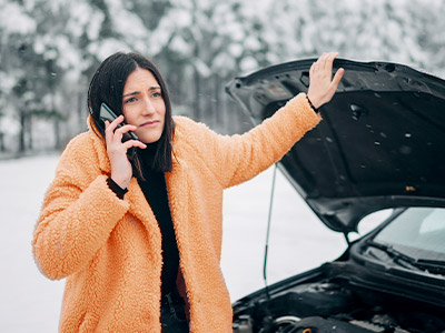 woman in orange on the phone with a car hood up in winter