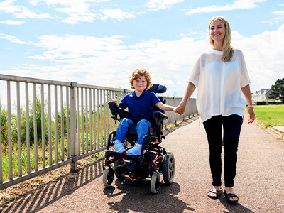 Child in a wheelchair holding a woman's hand