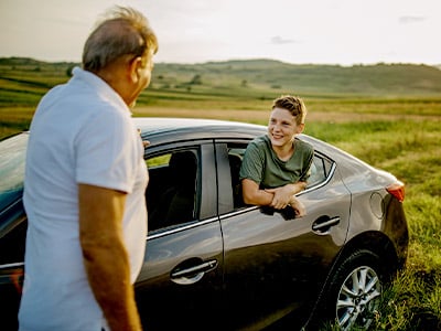 Kid hanging out of rear window of a car talking to older man