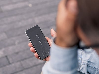 Man looking stressed at a phone with a broken screen
