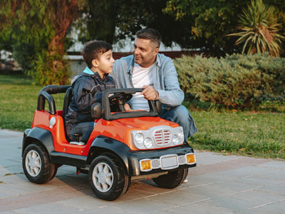 little boy in a toy riding car with father kneeling beside it