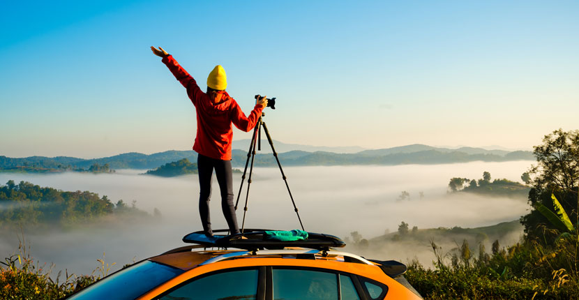 Person standing on top of an orange car with a camera on a stand looking out over a foggy landscape