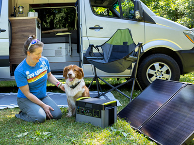 A woman and a dog sitting outside an RV with a Goal Zero power station and solar panel