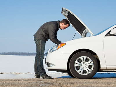 Man looking under the hood of a white car on the side of the road