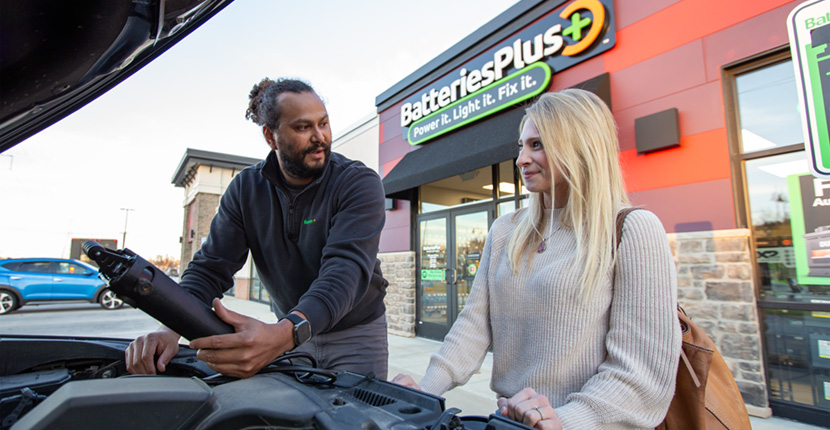 A store employee checking an auto battery while talking to the car owner.