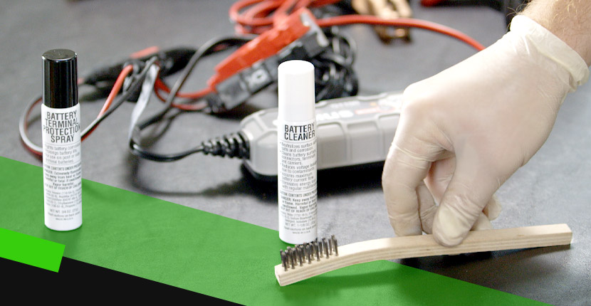 A person cleaning a battery with battery terminal spray and battery cleaner