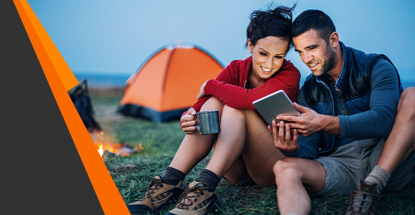 Man and a woman looking at a tablet while camping
