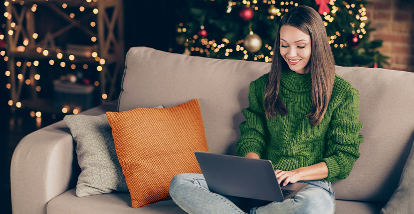 Woman in green sweatshirt sitting on a couch working on a laptop