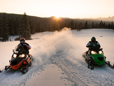 2 people riding snowmobiles in an open area