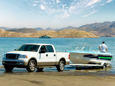 white pickup truck with a boat on a trailer near the water