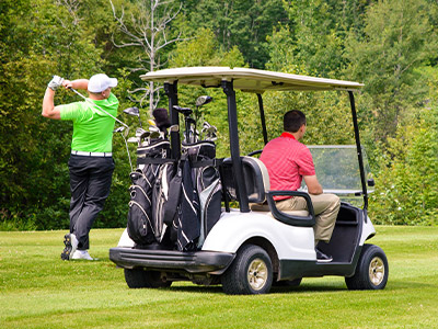 Golf cart on the green with one golfer taking a swing