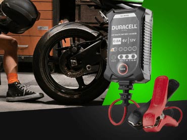 Man sitting on a bench wiping his helmet with the rear wheel of a motorcycle - close up of a Duracell battery charger