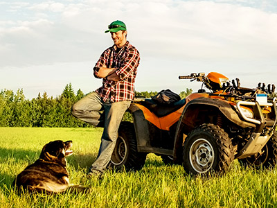 man leaning against an atv with dog in a field